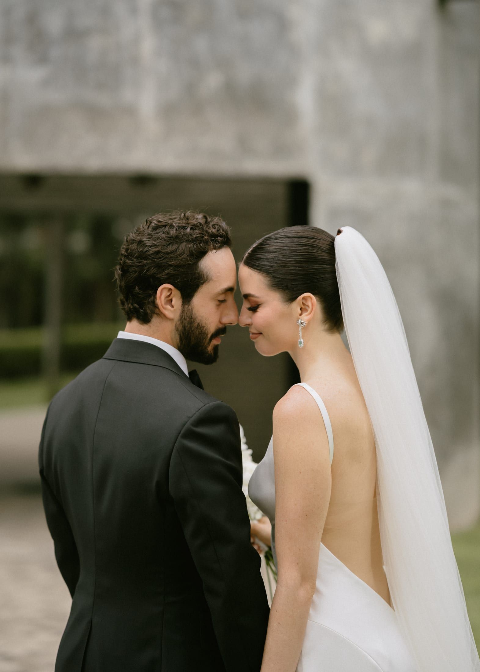 Los novios con las frentes juntas; ella con velo largo y él de esmoquin