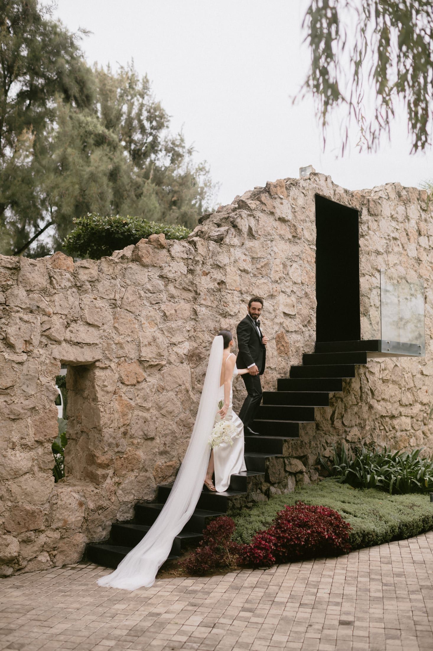 La novia sube una escalera de piedra con el velo largo cayendo por los escalones