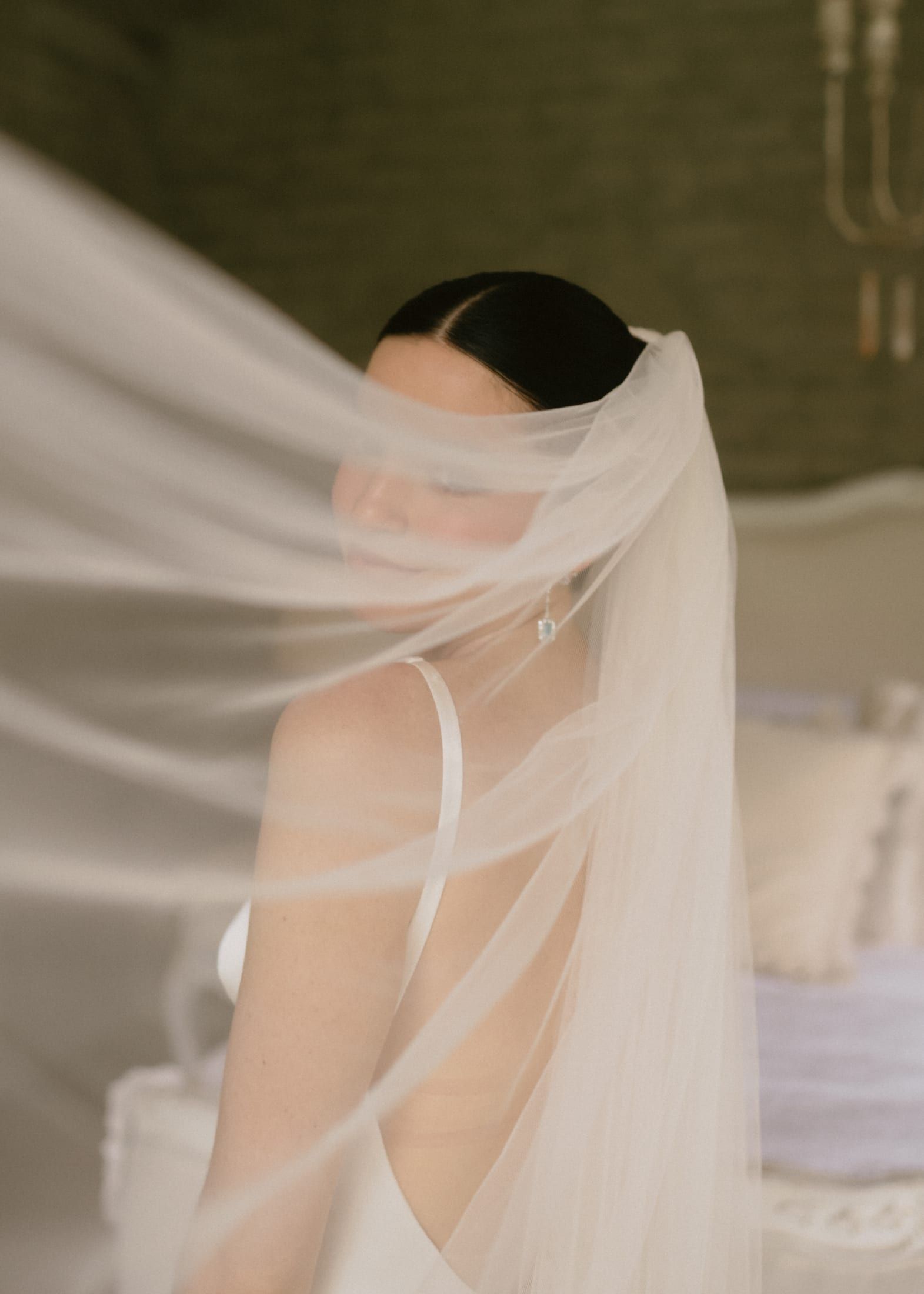 La novia de espaldas con el velo cubriéndole el rostro, con luz suave