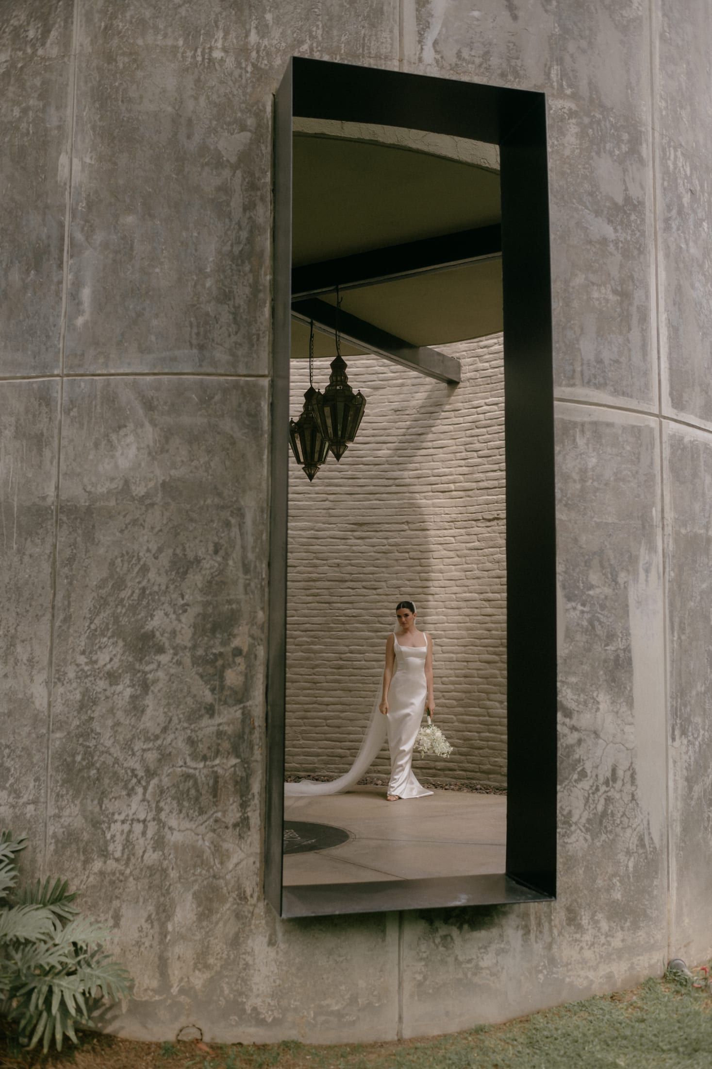 Reflejo de la novia en un espejo largo de marco negro sobre un muro de concreto