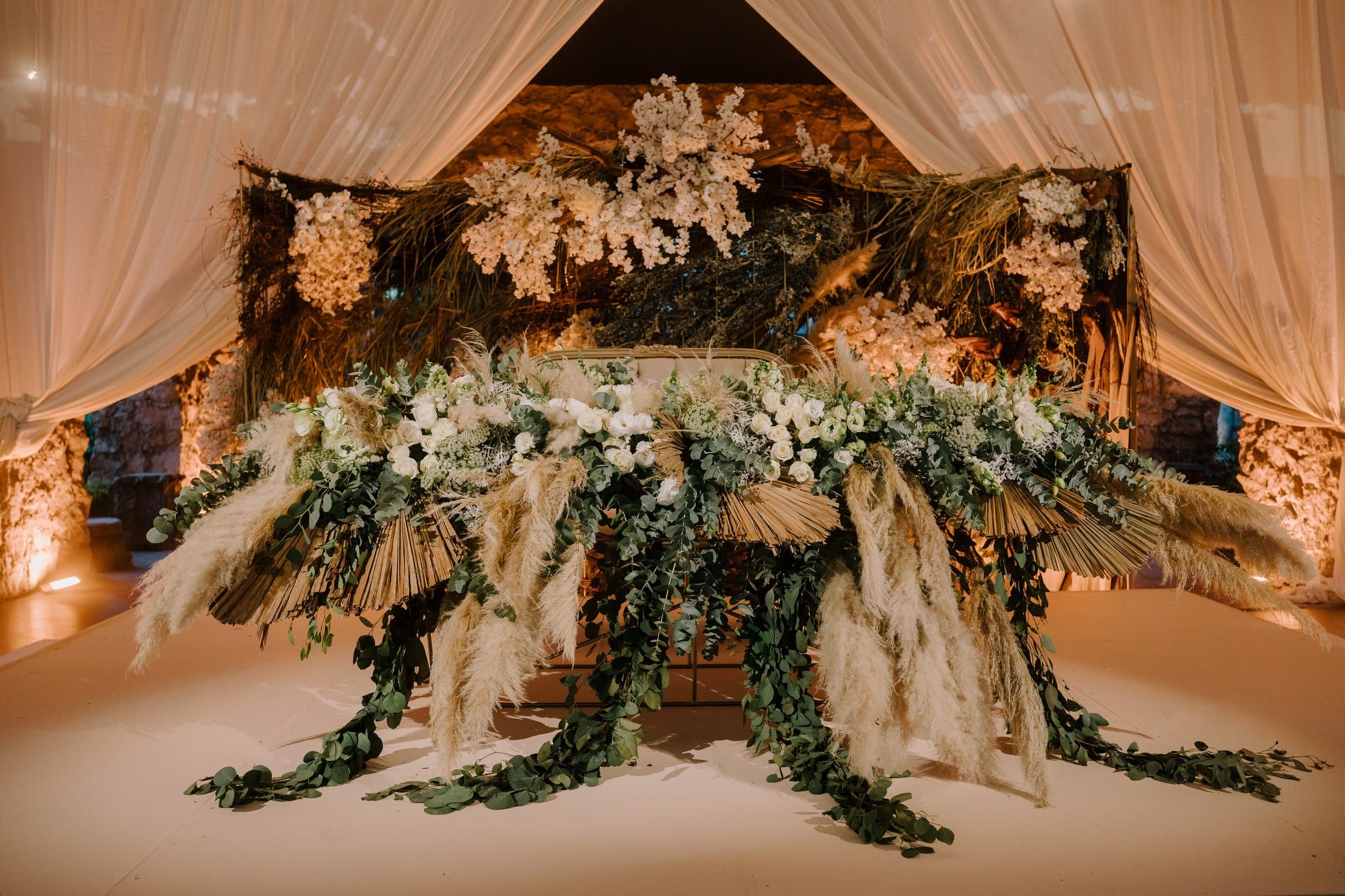 Mesa de novios con flores secas, pampas y follaje sobre una tarima blanca