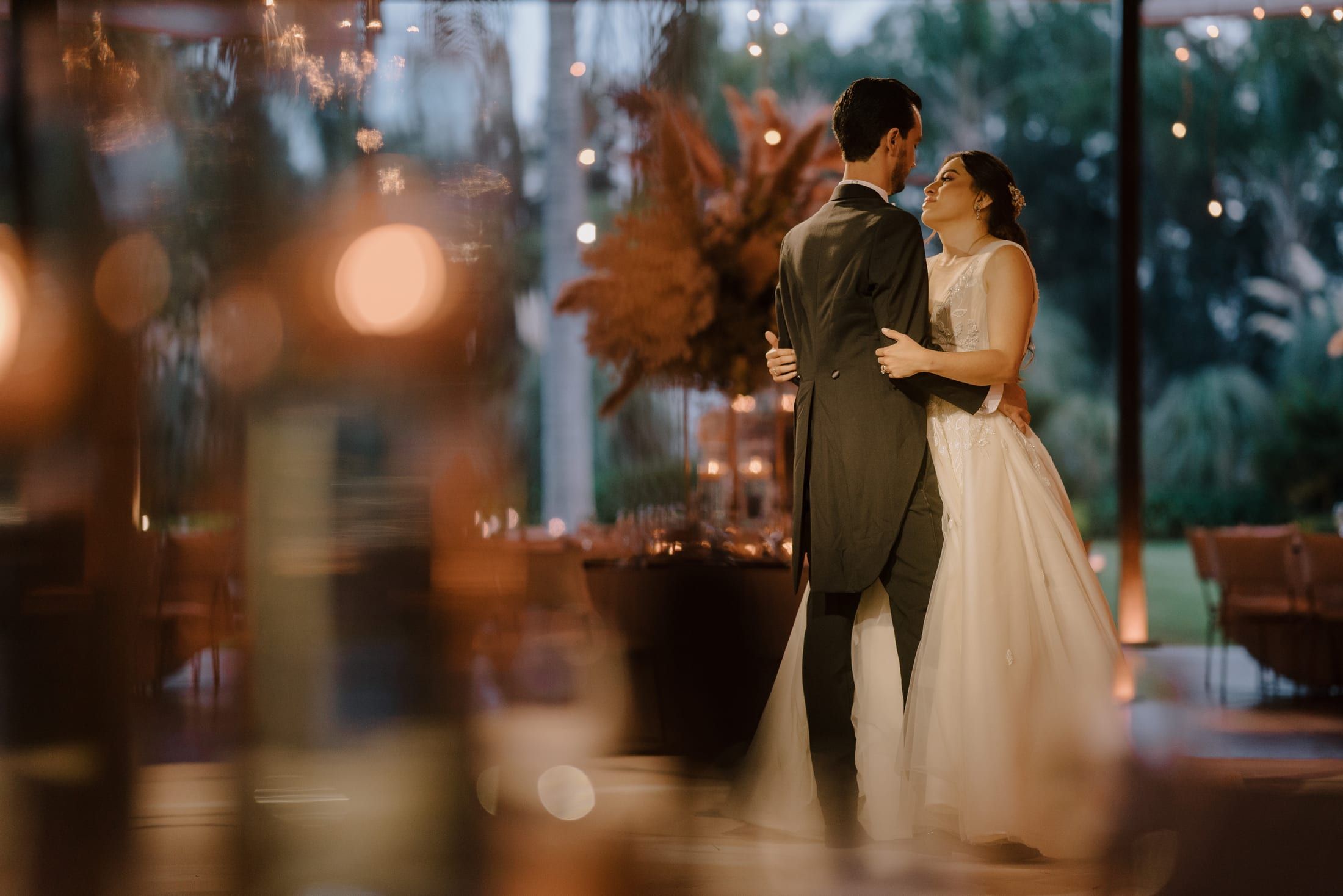 Los novios bailan con luces cálidas desenfocadas en primer plano