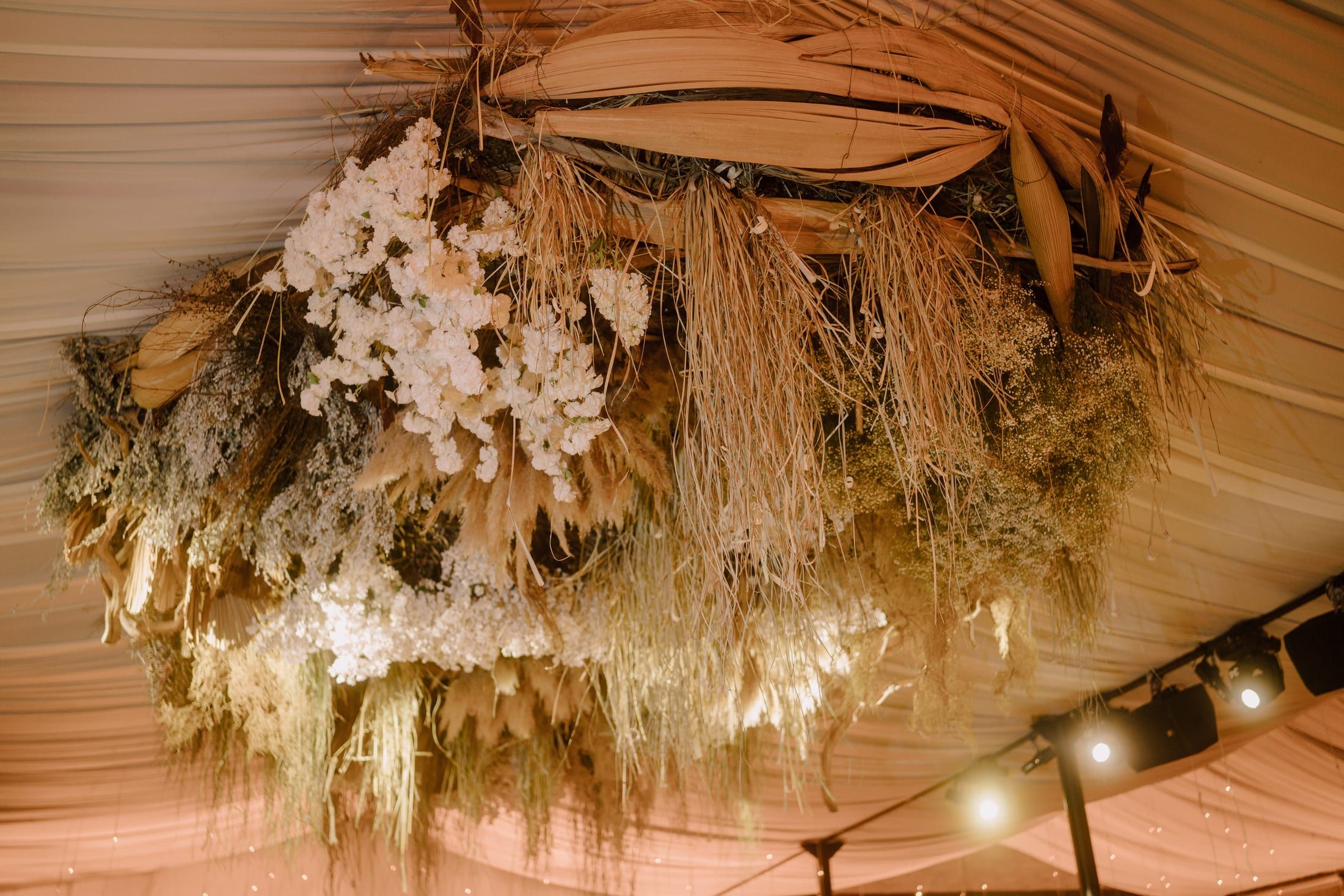 Instalación colgante de flores secas y orquídeas sobre la pista, con luces