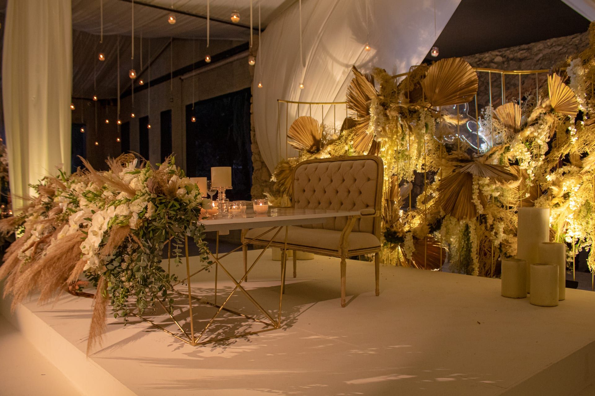 Mesa de novios con sillón tapizado y arreglos de flores secas y pampas sobre una tarima
