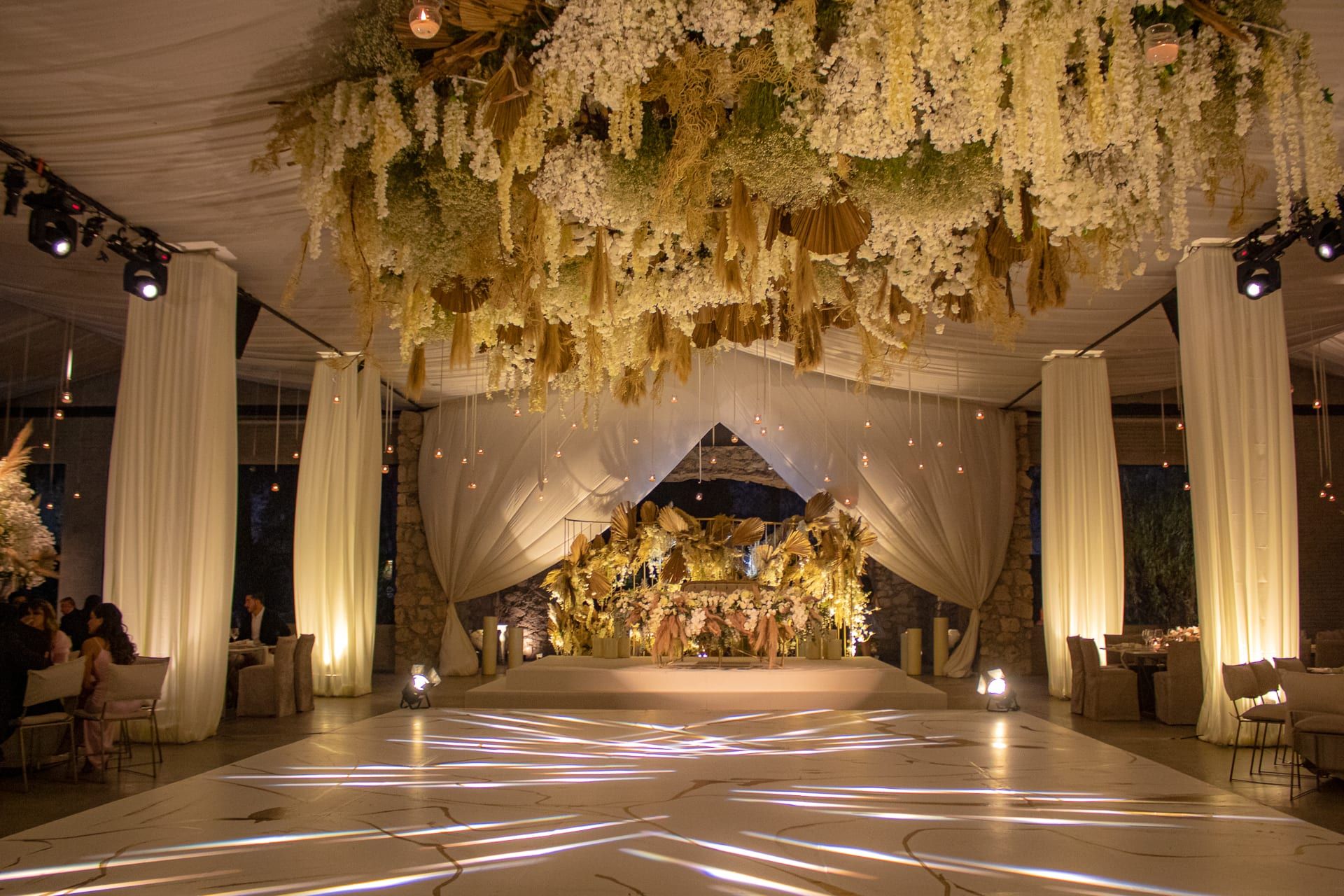 Salón con techo de flores blancas colgantes, cortinas de tela y pista iluminada