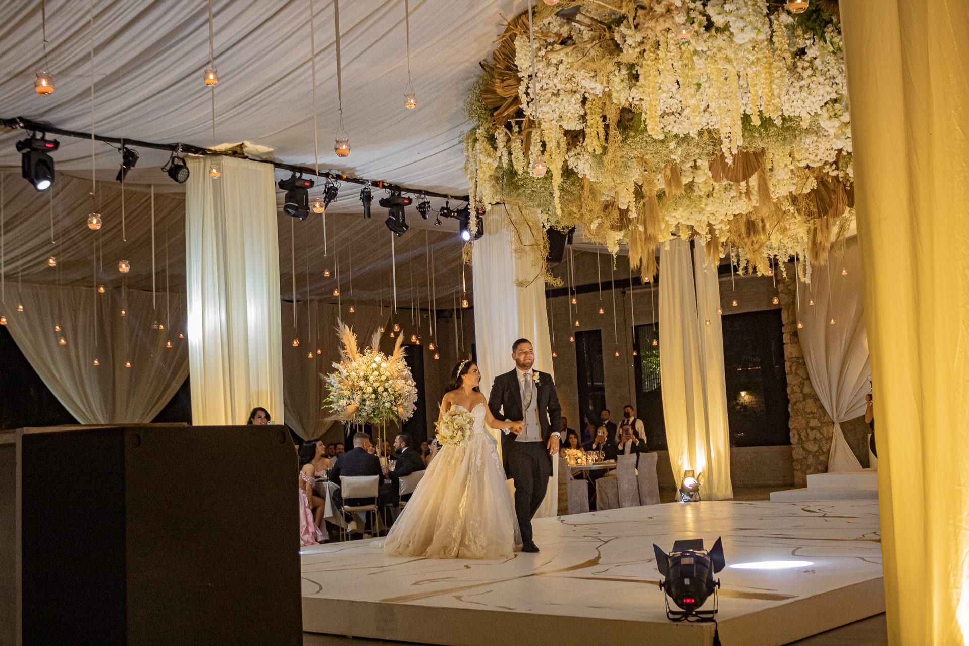 Los novios caminan hacia la pista bajo un techo de flores y luces