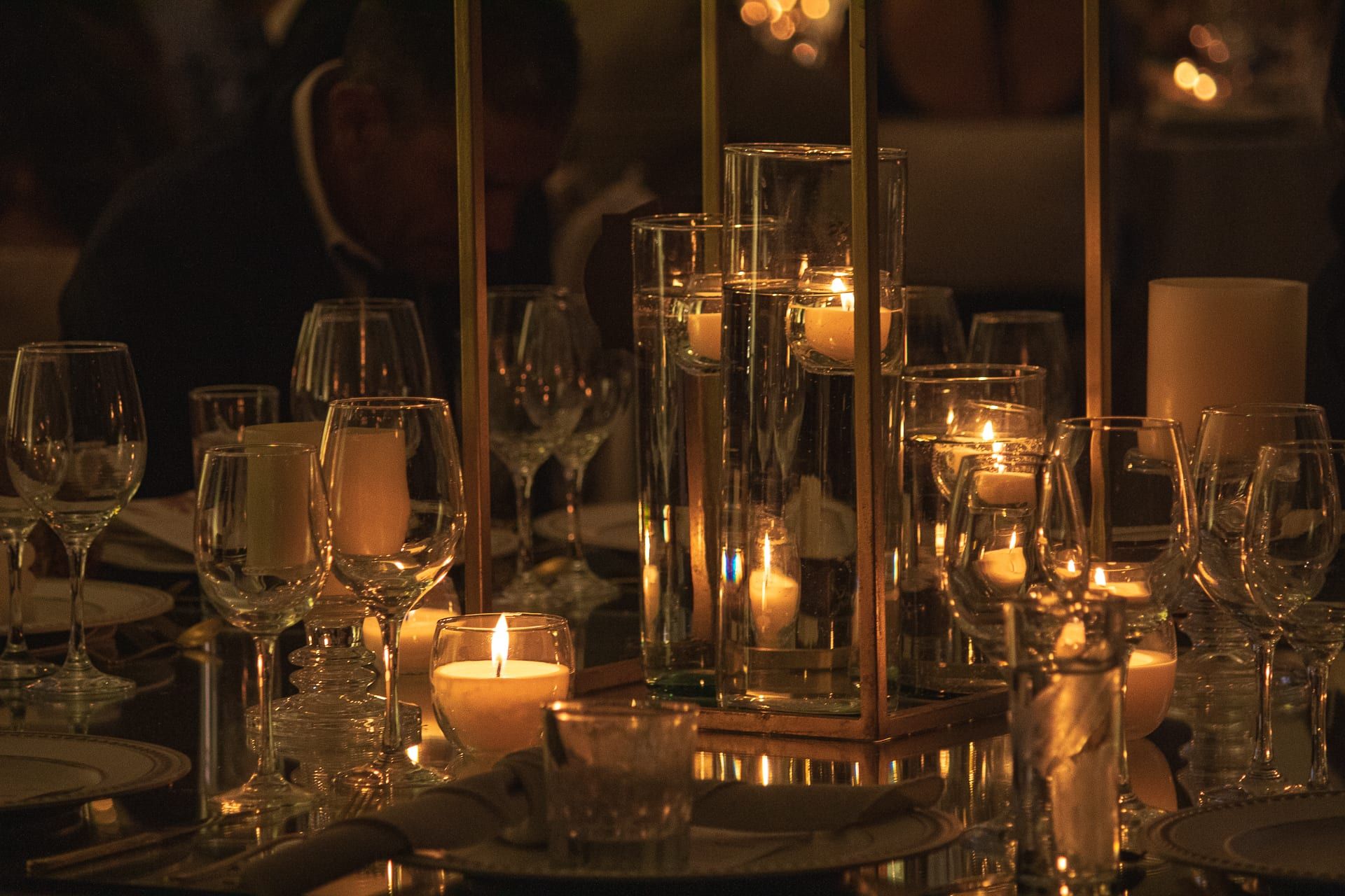 Velas y cilindros de vidrio con flores sobre la mesa, con invitados al fondo