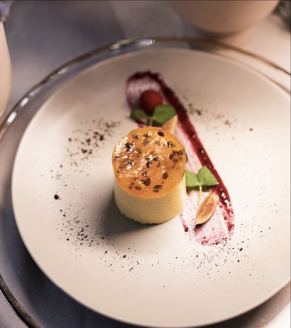 Postre cilíndrico dorado con trazo de salsa roja y frutos rojos sobre un plato claro