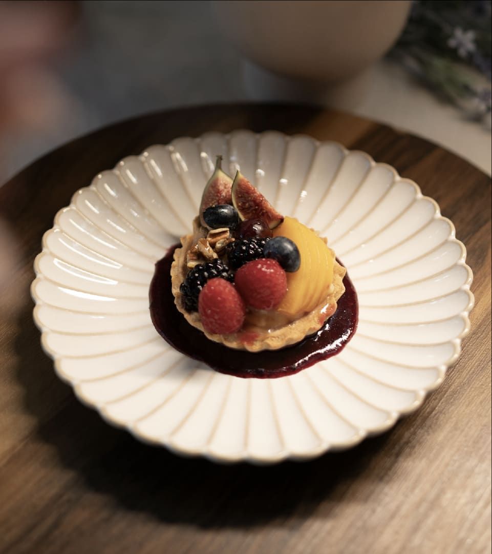 Tarta de frutos rojos con higo sobre salsa oscura, servida en un plato blanco acanalado