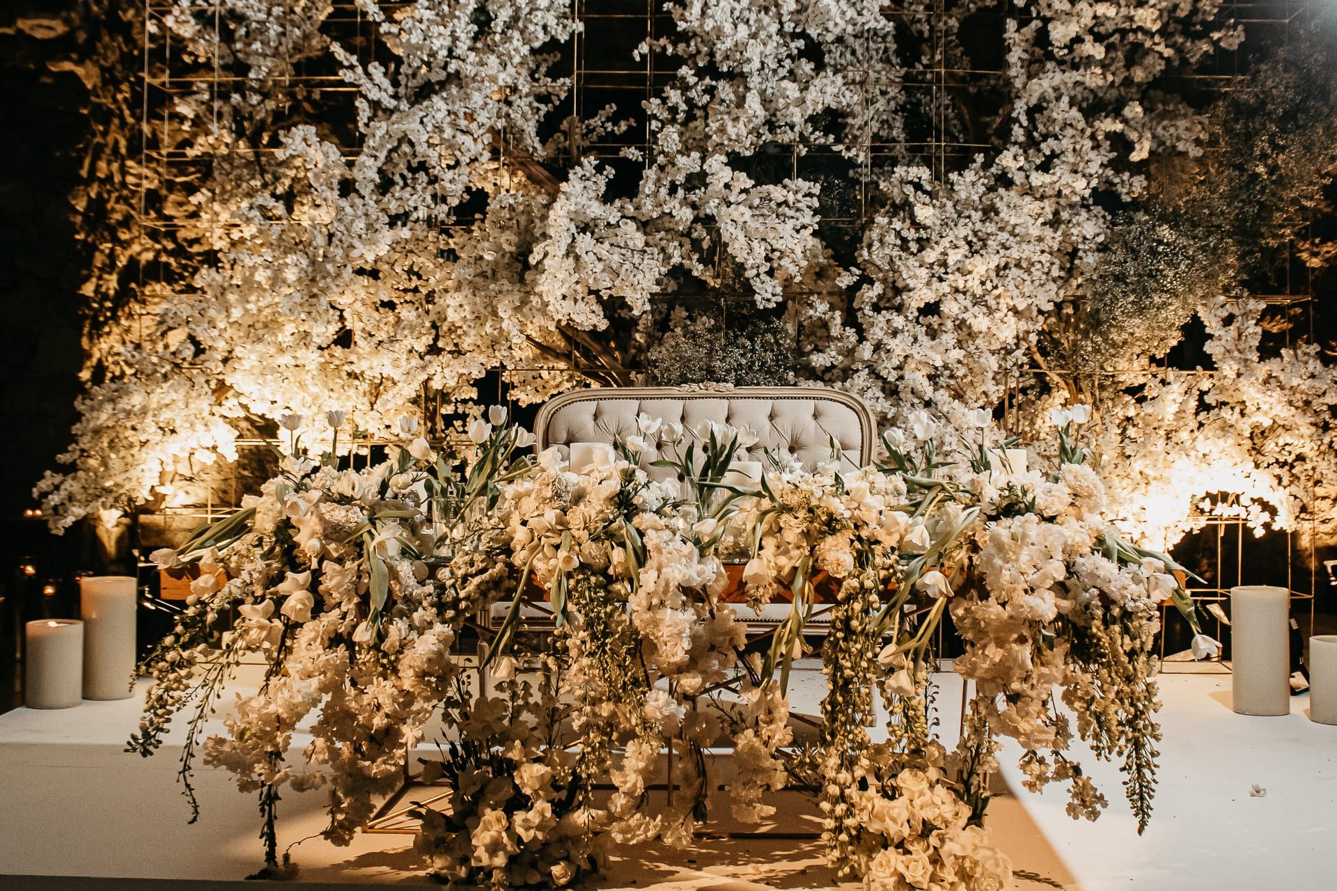 Instalación de flores blancas en cascada sobre un sillón de novios, con luz cálida