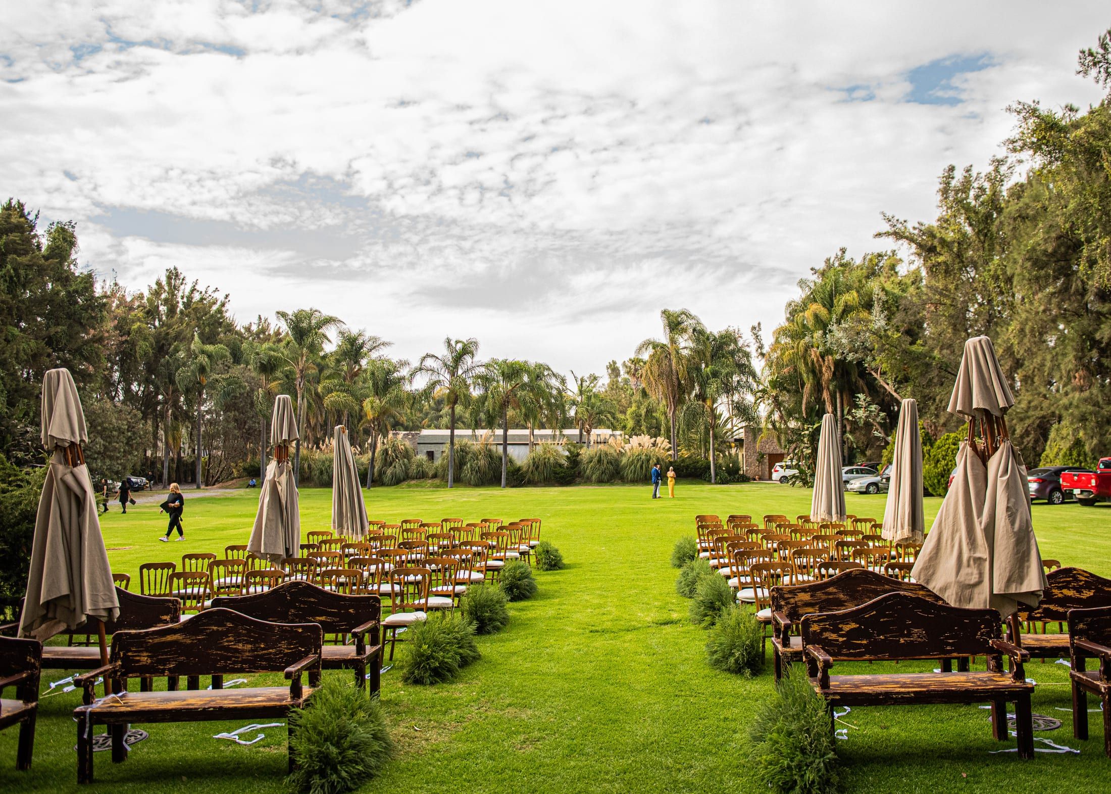 Jardín amplio con sillas y bancas de madera para una ceremonia al aire libre, entre palmeras