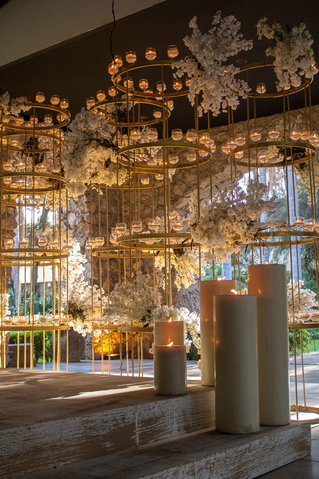 Candil de flores y hojas colgando en el salón, junto a velas altas y ventanales