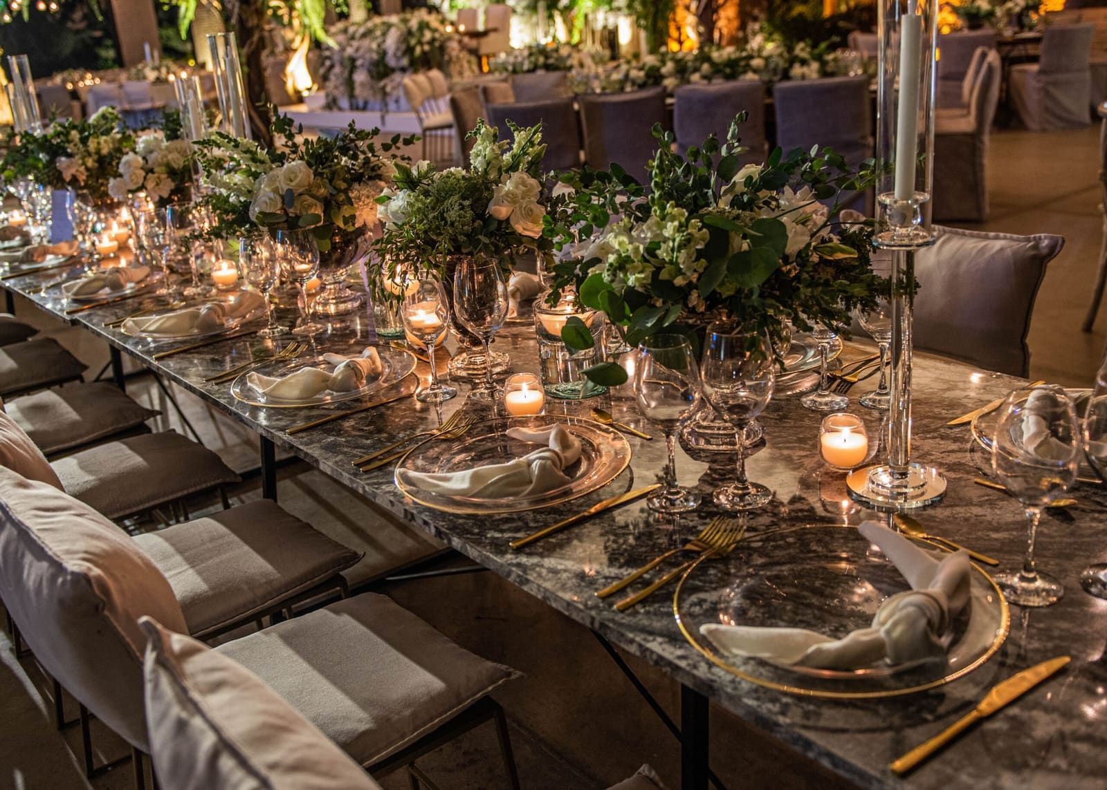 Larga mesa de banquete con vajilla de borde dorado, copas, centros de mesa verdes y blancos, y velas