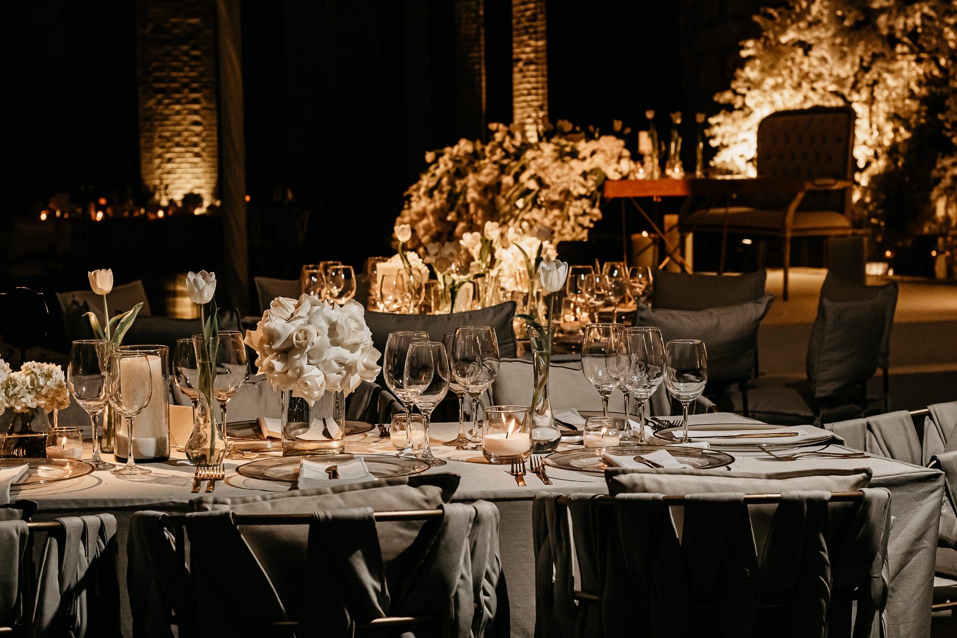 Mesas largas con arreglos de flores blancas y tulipanes en el salón, de noche