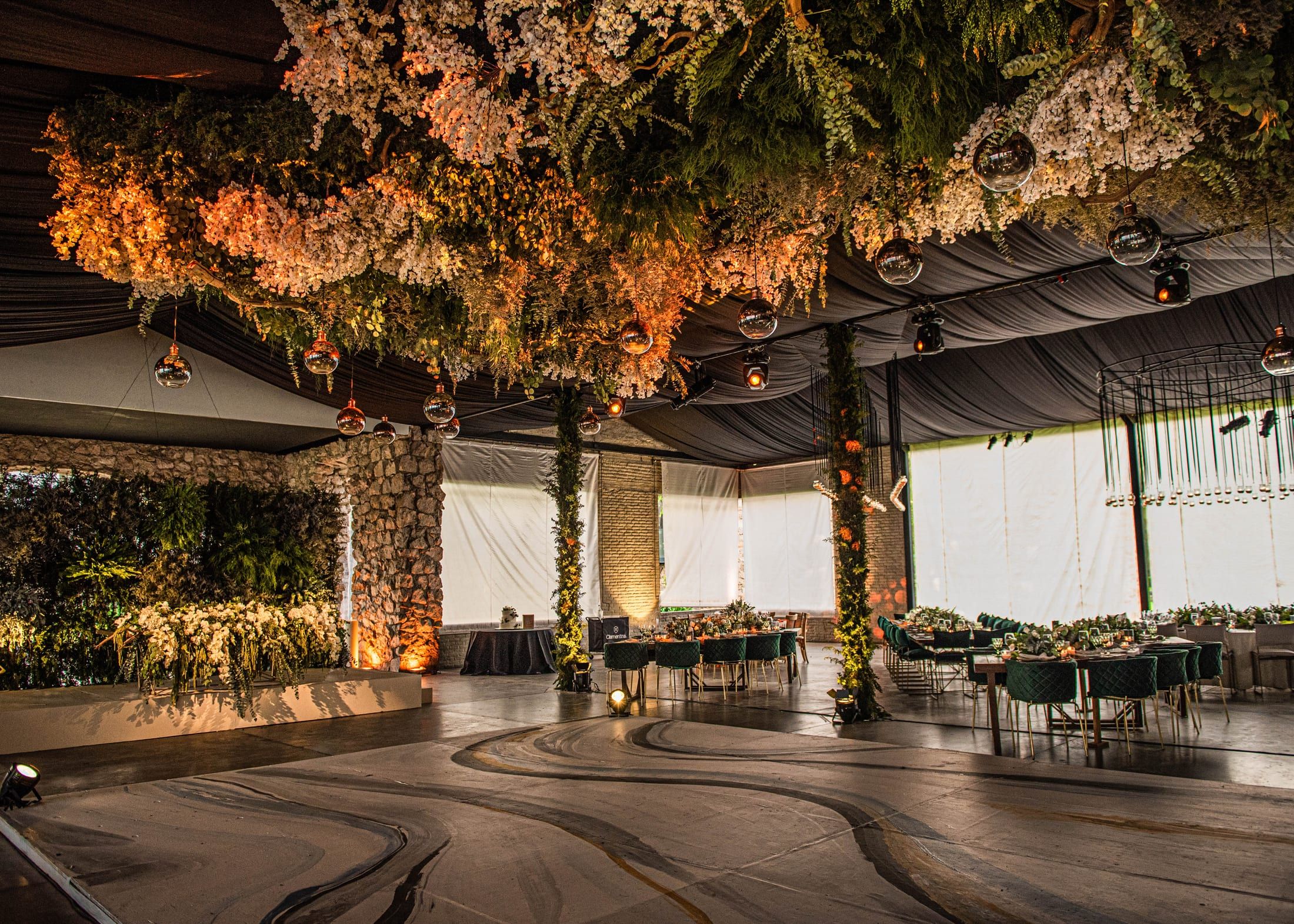 Salón de noche con un techo cubierto de flores y follaje, pista de baile y mesas al fondo