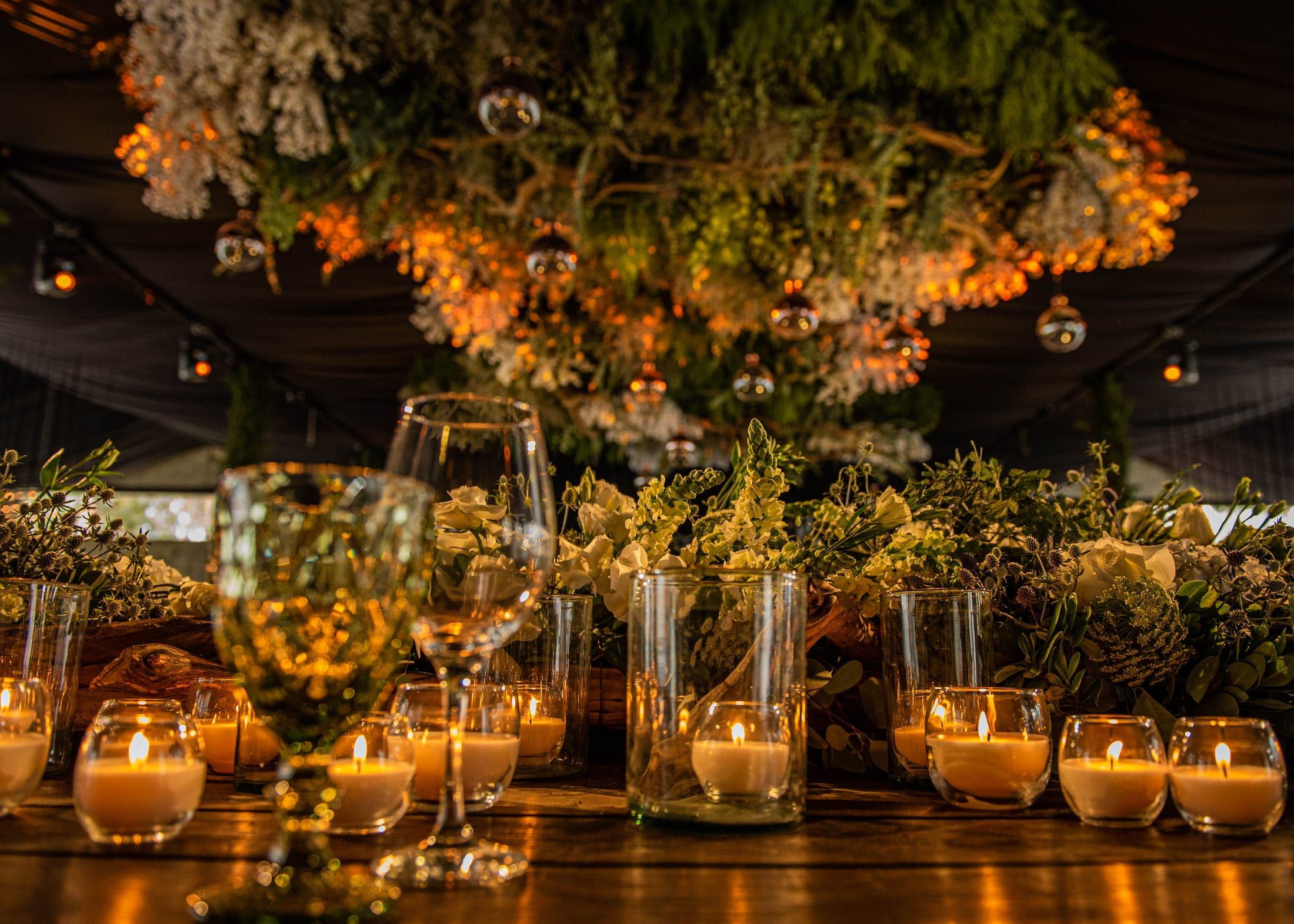 Techo de flores y follaje sobre una mesa con velas, copas de cristal y esferas de vidrio