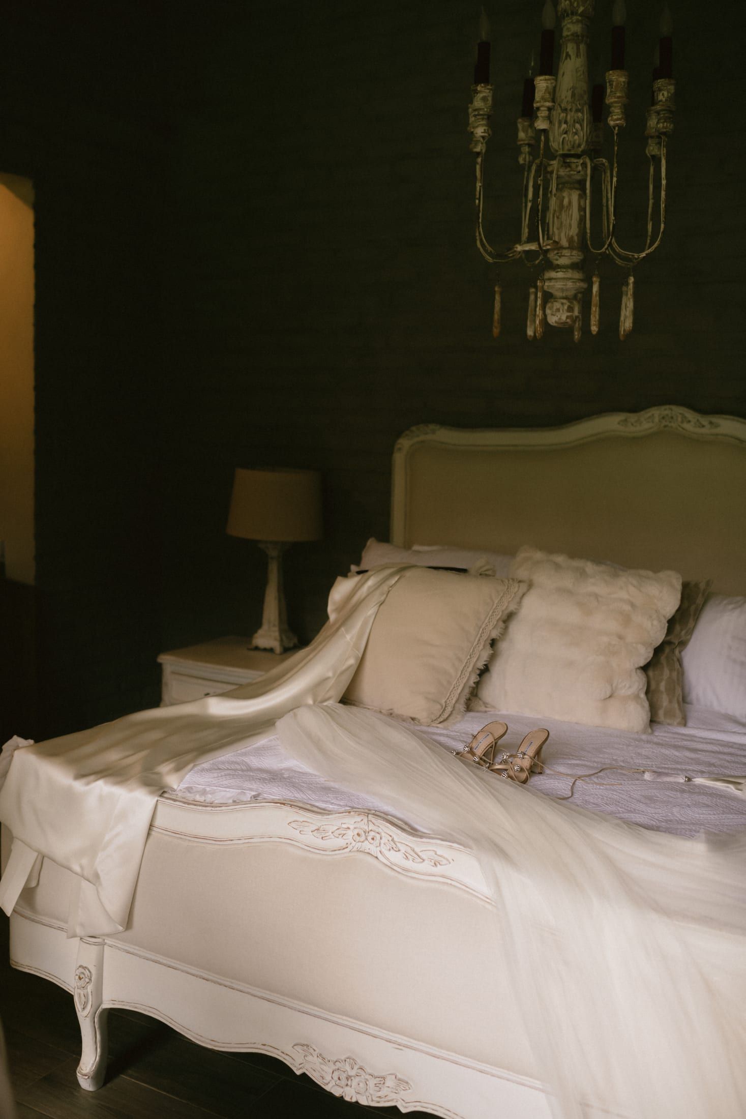 Cama blanca de madera tallada junto a un espejo de marco blanco y una lámpara, en la suite