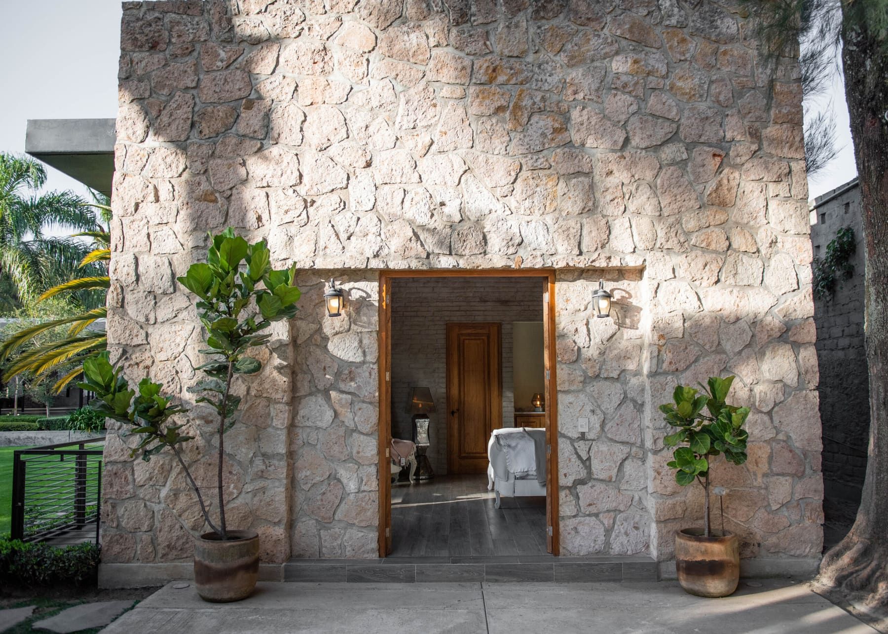 Entrada de piedra de la suite, con puerta de madera y dos macetas de hoja grande