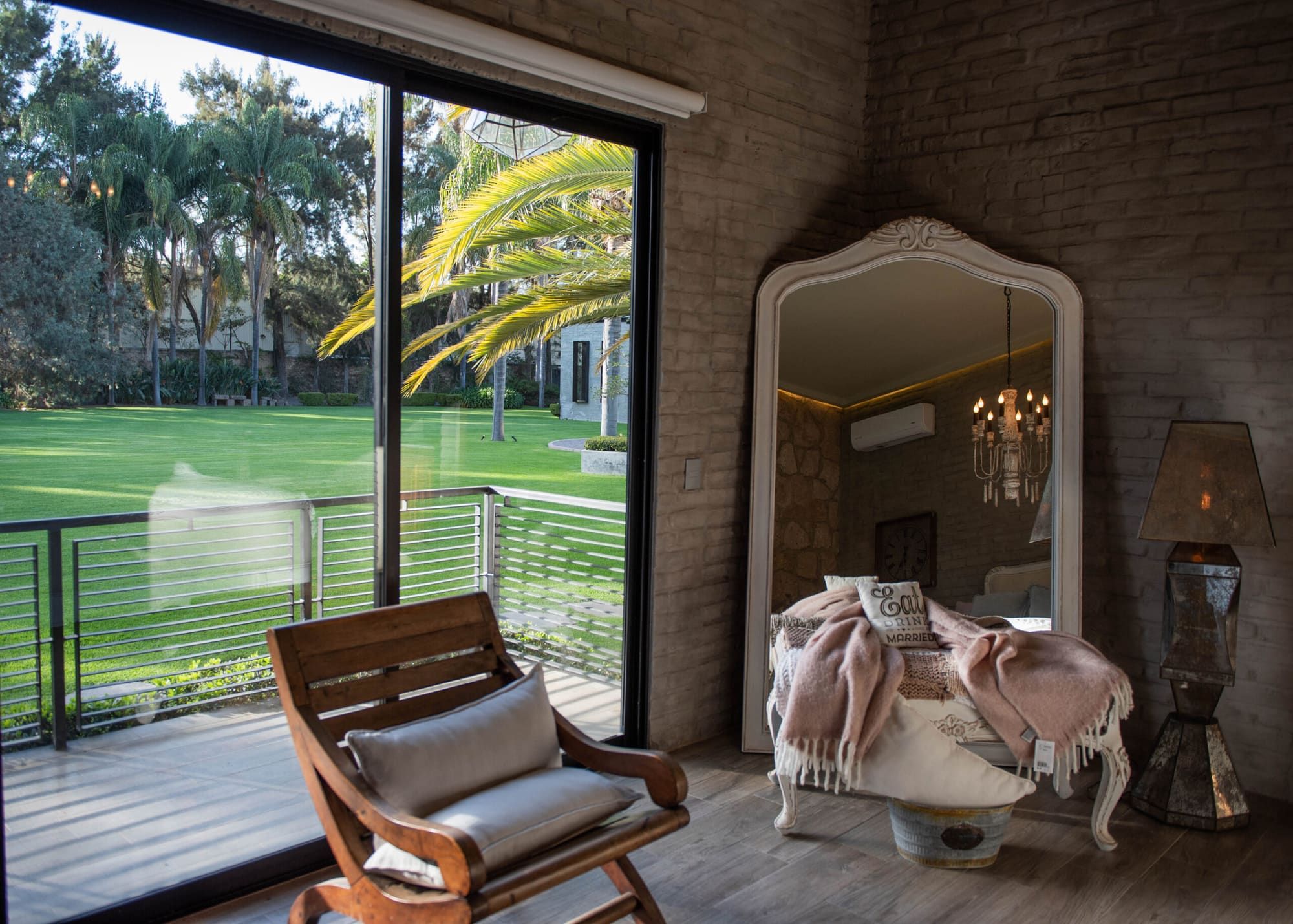 Suite con ventanal hacia el jardín, silla de madera con cojín y espejo con una manta rosa